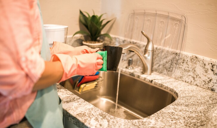 Cleaning woman washing a coffee cup with pink cleaning gloves