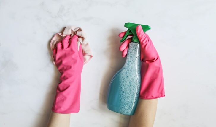 cleaning person wearing pink gloves wiping a dirty surface with a soft pink cloth