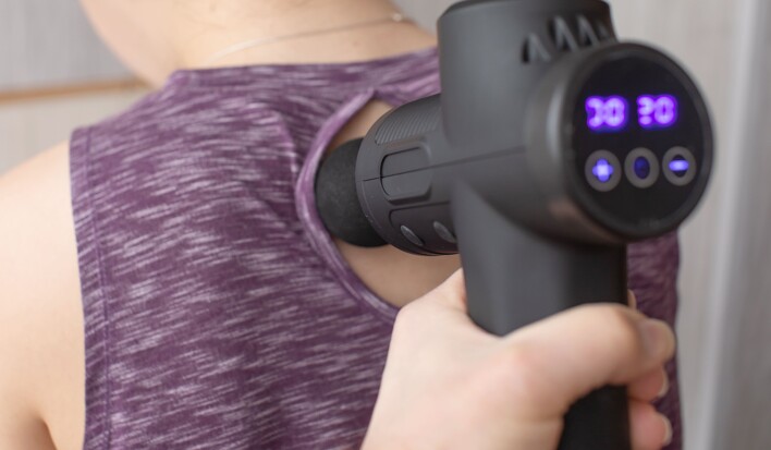 Woman applying massage gun to back
