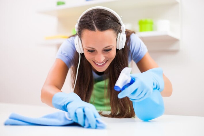 woman cleaning surface while listening to music through headphones