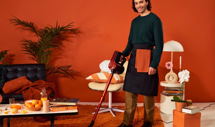 Professional cleaning man cleaning and vacuuming an orange living room