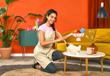 Une femme de ménage qui nettoie une table de salon avec un plumeau.