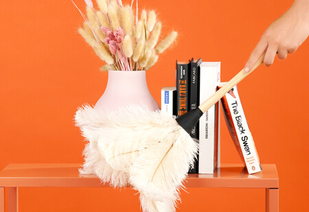 Regular cleaning - a housekeeper is dusting a shelf with book and a flower vase