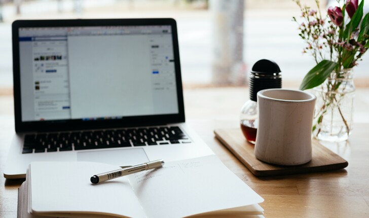 Office desk with coffee mug, flowers, notebook and computer